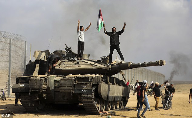 Palestinians wave their national flag and celebrate by a destroyed Israeli tank in the Gaza Strip