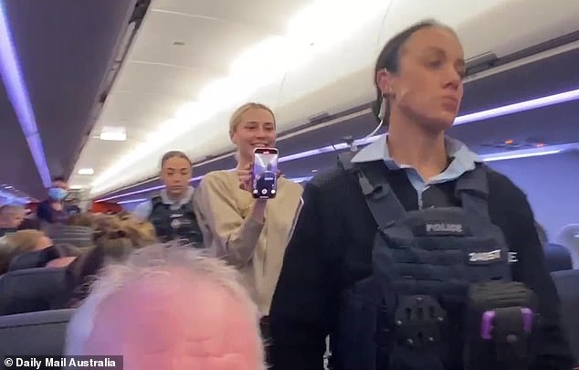 Flanked by AFP officers, the woman was seen strutting confidently down the aisle, waving at fellow passengers and smiling for cameras as she filmed the dramatic moment on her phone