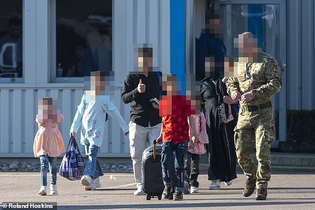 A soldier escorts a family at Stansted on May 23 as part of a government scheme costed at £7billion smuggling migrants TO Britain after a data-leak blunder exposed by the Daily Mail