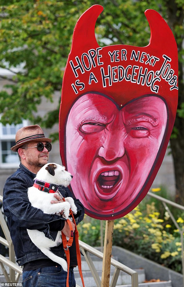 A man with a dog stands next to a placard, as anti-Trump demonstrators gather during a rally organized by the campaign group Stop Trump Coalition, protesting Trump's visit