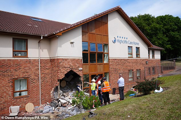 Workmen inspecting a hole that was smashed into the side of a care home after a car collided with it during a police chase