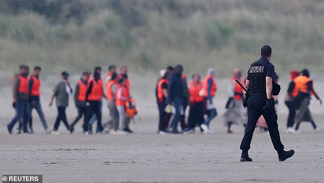 French police try to stop a group of migrants as they walk on the beach in an attempt to get on an inflatable dinghy to cross the English Channel to reach Britain