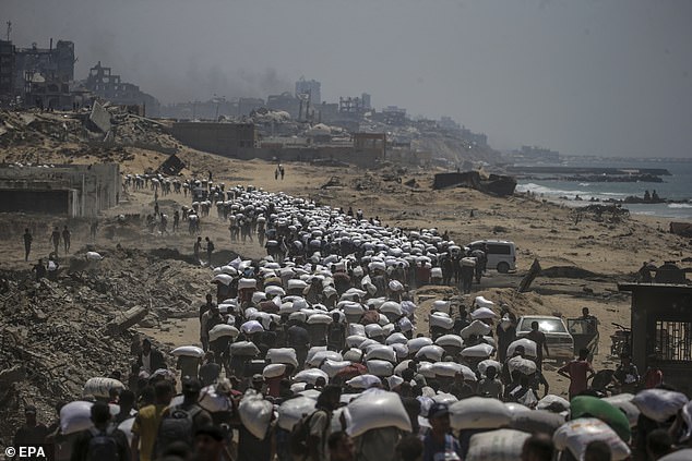 Internally displaced Palestinians carry bags of flour near a food distribution point in Zikim, northern Gaza Strip, 27 July 2025