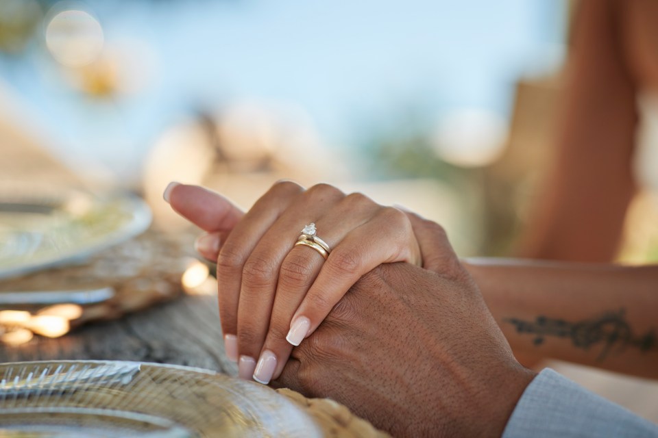 Bride with wedding ring holding hand of groom at table in winery