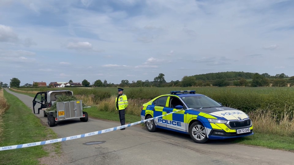 Police car blocking a road; a police officer stands nearby.