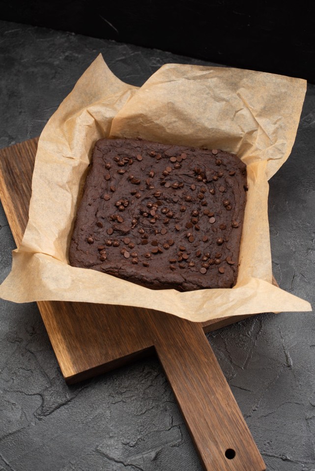 2F2AEKC Uncutted brownies with choco drops in baking paper on dark plaster background high angle view