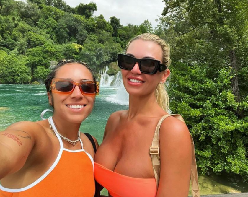Two women wearing sunglasses in orange tops in front of a waterfall.