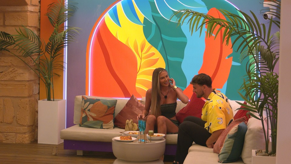 Two Love Island contestants talking on a sofa.