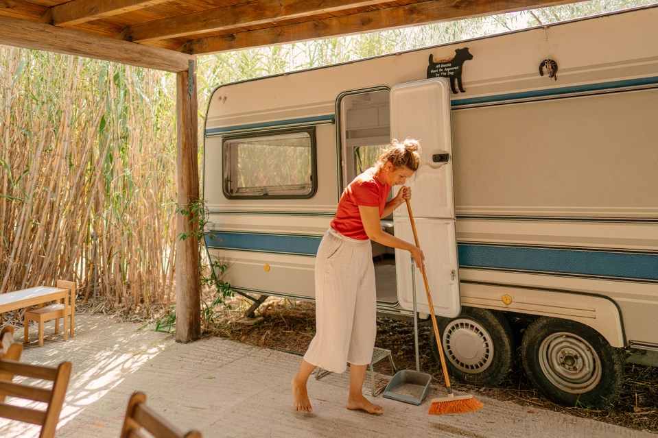 Woman sweeping patio outside camper van.
