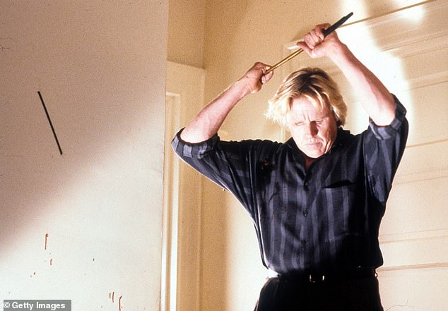 Busey is pictured raising a weapon in a scene from the film Hider in the House in 1989