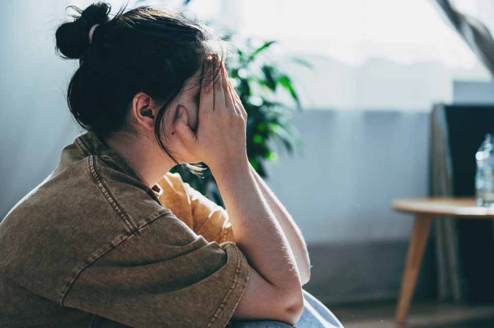 Upset teenage girl sitting on the floor, hands covering her face.
