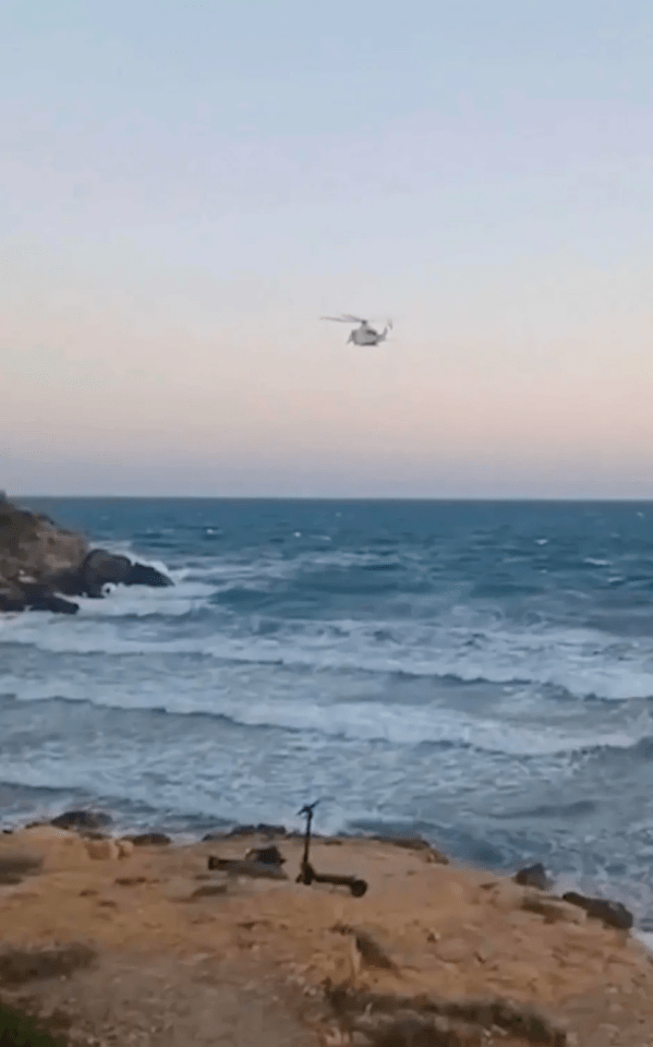 Helicopter over ocean near rocky shore with scooter.