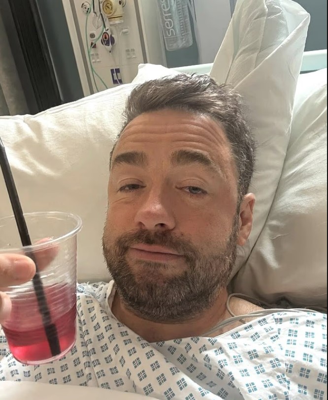 Man in hospital bed holding a drink.