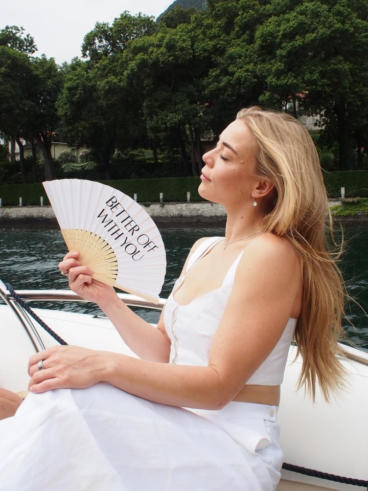 Woman on a boat holding a hand fan that says "Better Off With You."