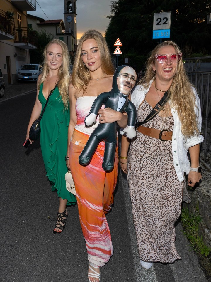 Three women walking down a street, one carrying an inflatable caricature.