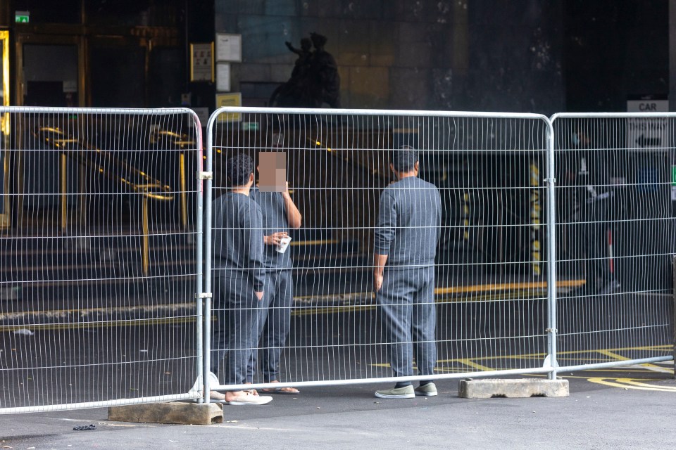 Three men stand behind a temporary fence outside a hotel.