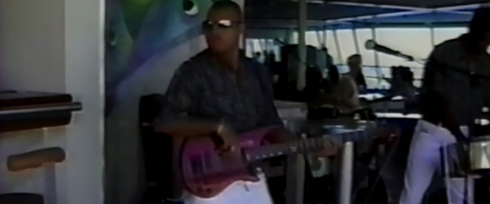 Man playing a pink guitar on a ship.