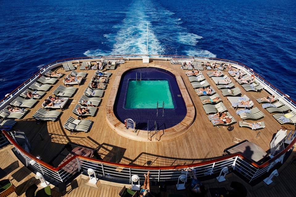 Aerial view of a ship's deck with a pool and sunbathers.