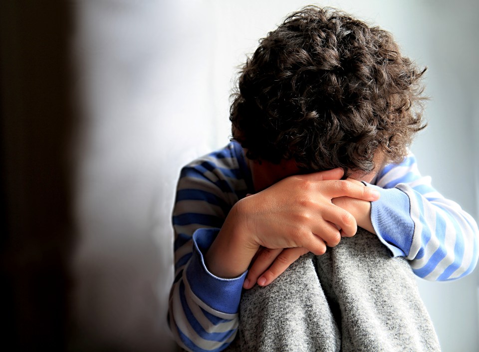 A young boy sits alone, crying and hugging his knees.