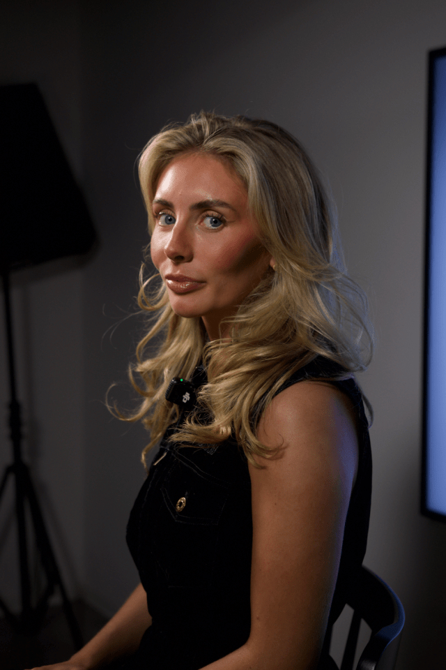 Woman with blonde hair, wearing a black sleeveless top, looking over her shoulder.