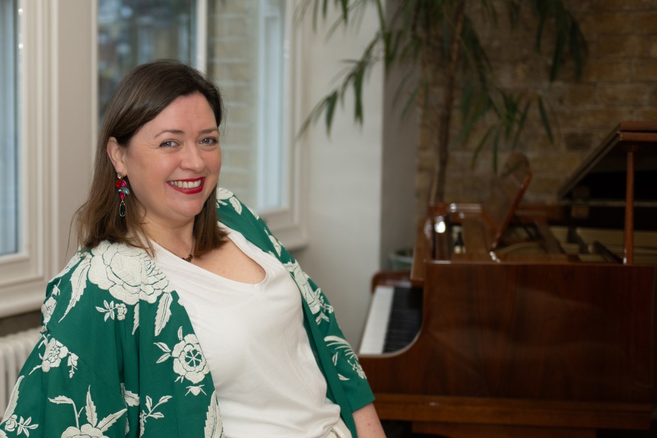 Portrait of a smiling woman wearing a green floral kimono and white shirt, sitting near a piano.