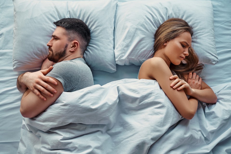 A young couple lies in bed turned away from each other.