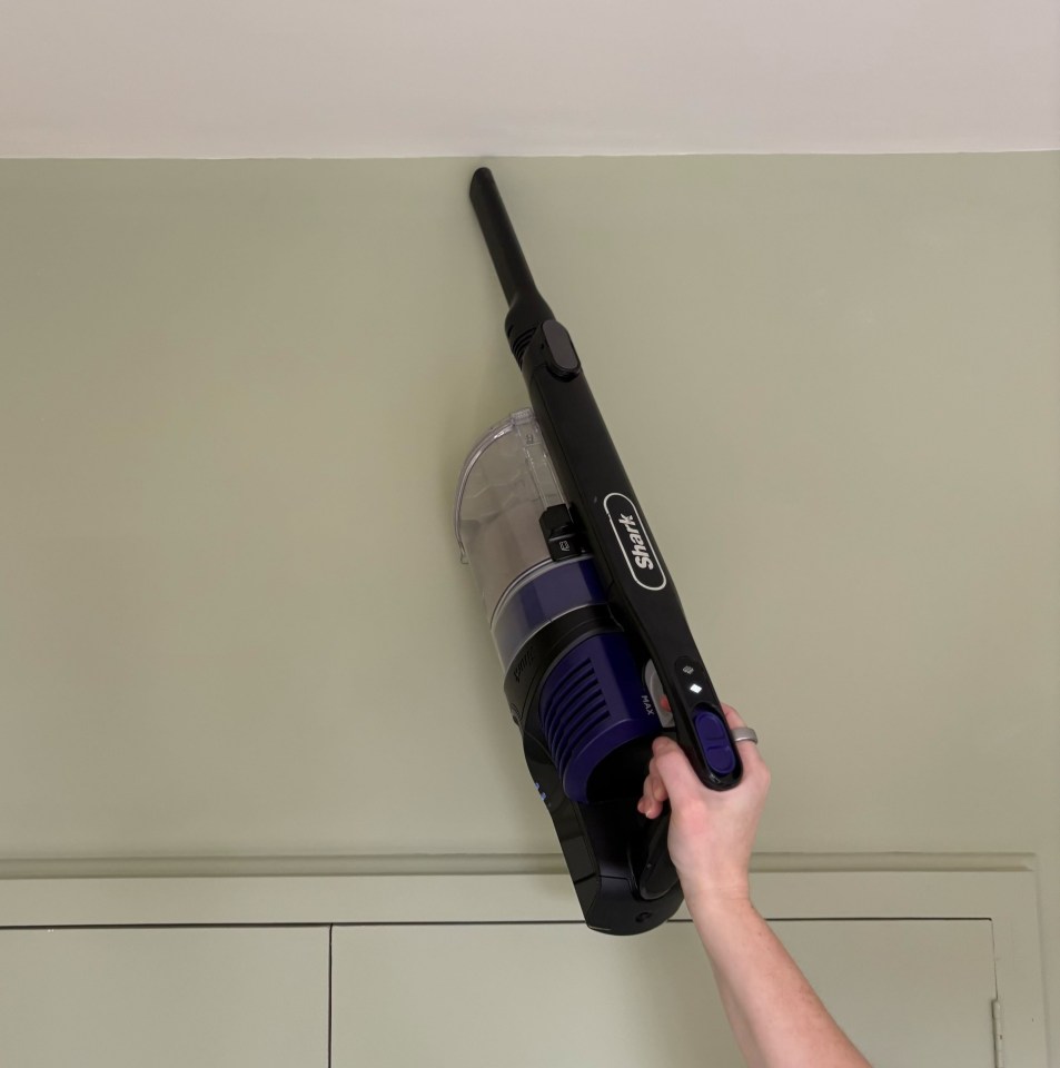 A hand holding a Shark IZ202UKT vacuum cleaner against a wall.