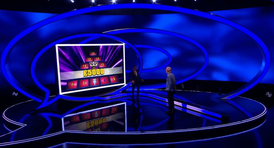 Game show set with two contestants and a large screen displaying a pyramid of numbers and a £5000 prize.