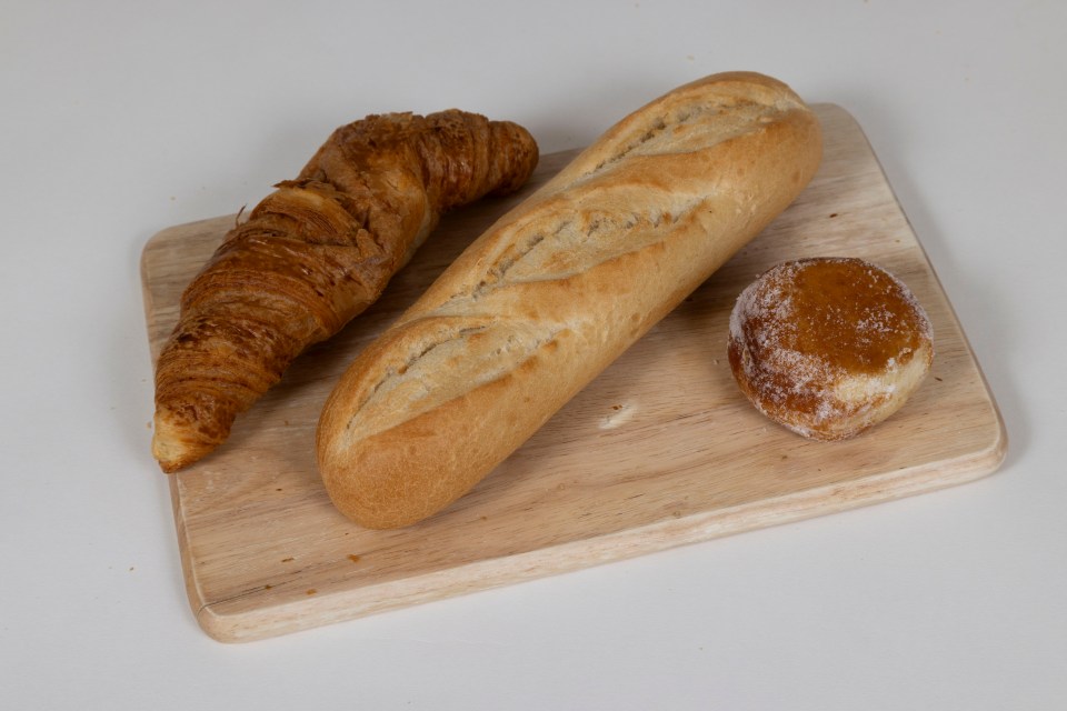 Croissant, baguette, and bun on a wooden cutting board.