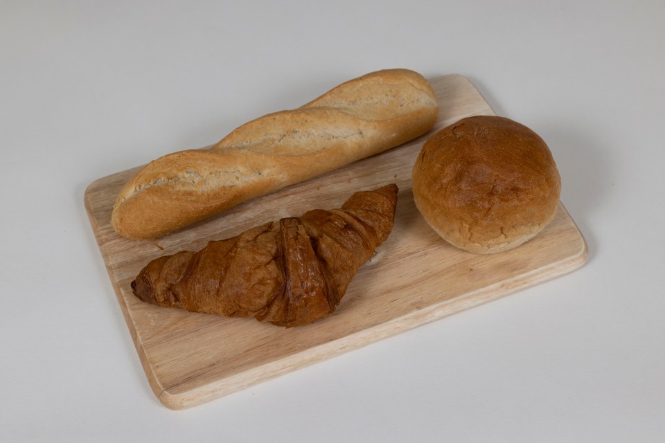 Baguette, croissant, and bun on a wooden cutting board.