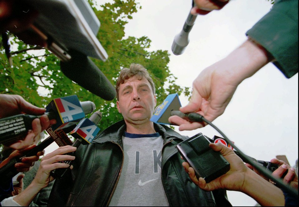 A man surrounded by reporters and microphones speaks to the press.