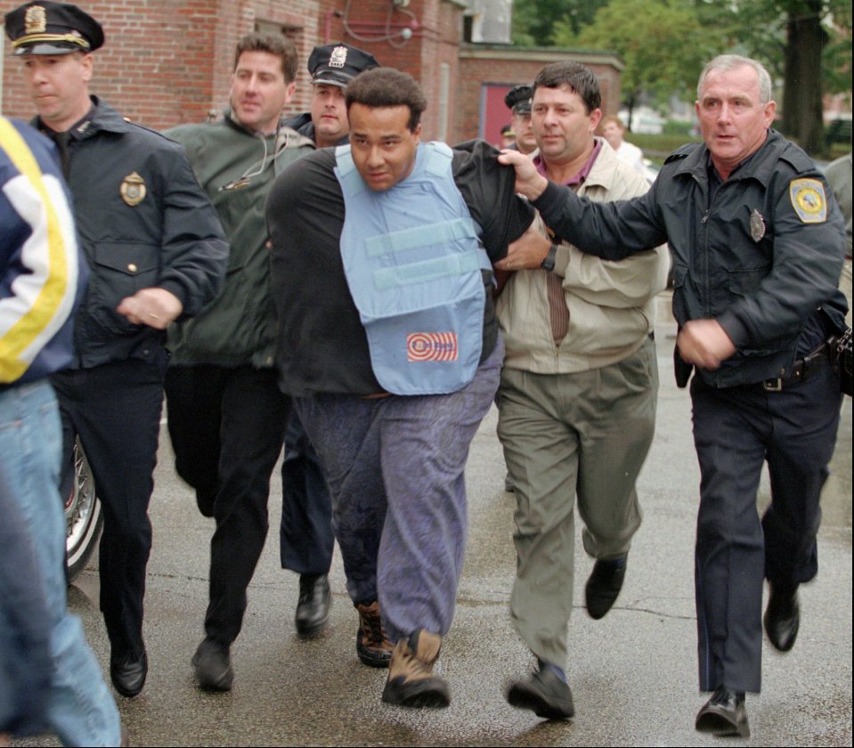 Charles Jaynes, wearing a bullet-proof vest, escorted by police officers.