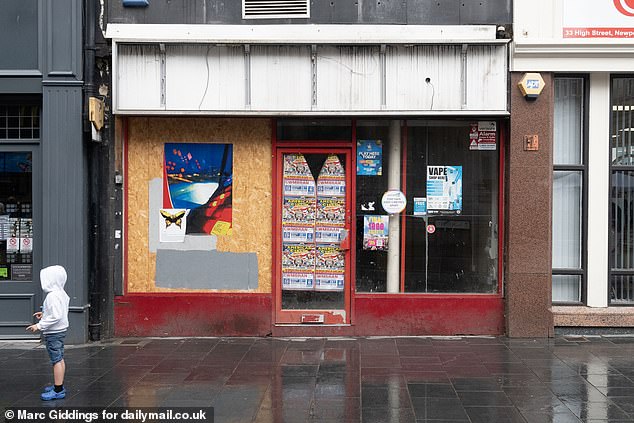 A boarded up shop with posters including one advertising vapes plastered across it
