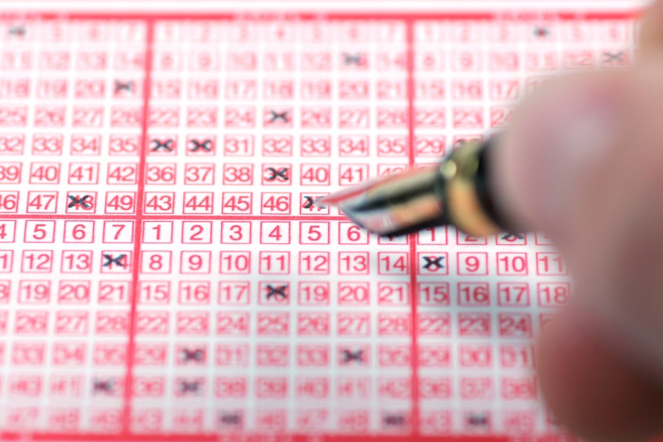 A hand using a pen to mark numbers on a lottery ticket.