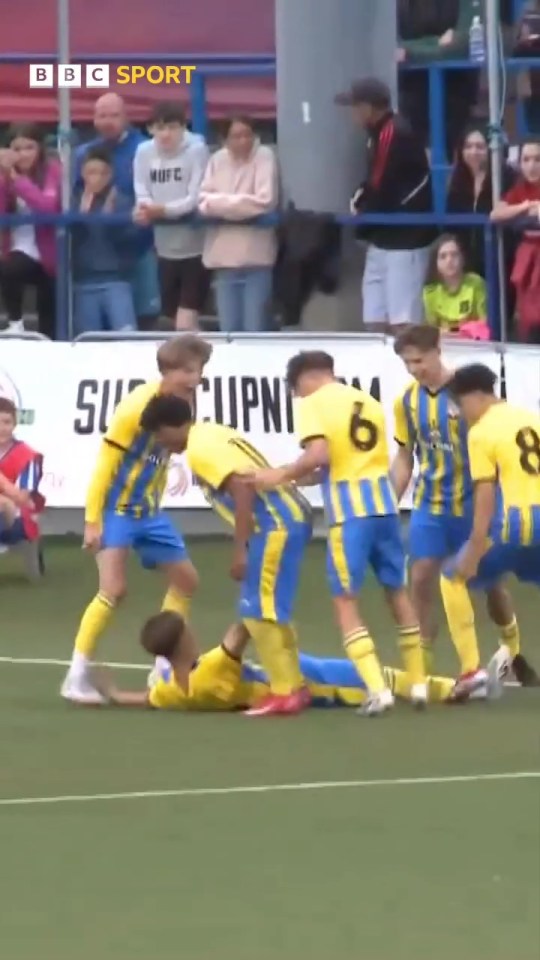 Soccer players celebrating after a goal while one player lies on the ground.