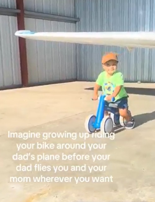 Toddler riding a tricycle in front of a small plane.