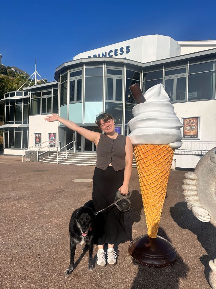 Person with dog standing near a giant ice cream cone in front of a building.