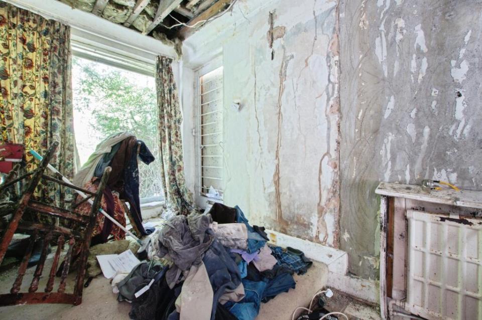 A cluttered room with mold-damaged walls and a pile of clothes on the floor.