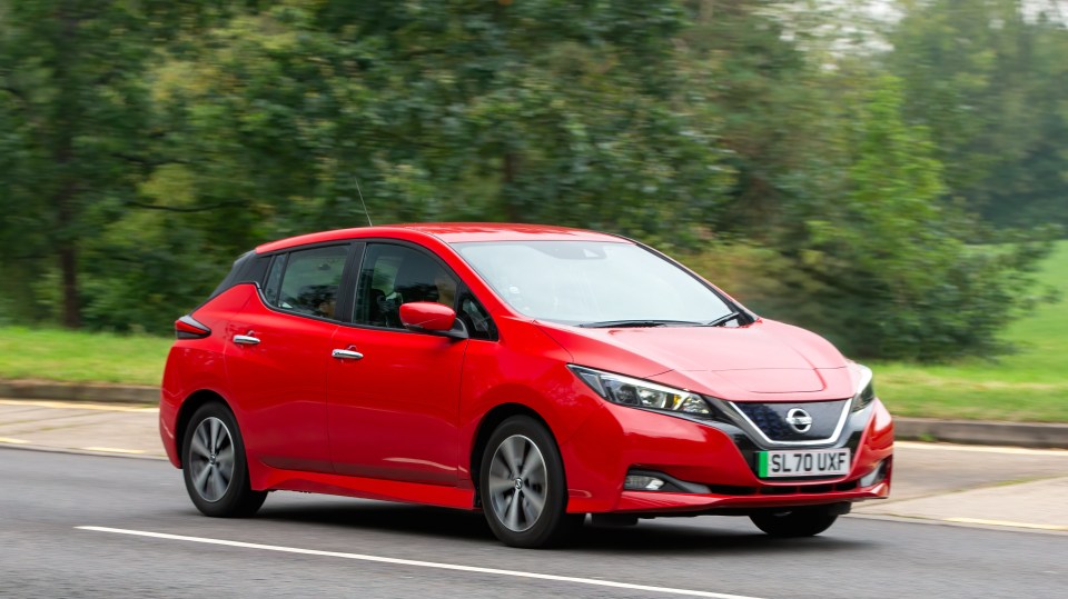 Red Nissan Leaf electric car driving on a road.