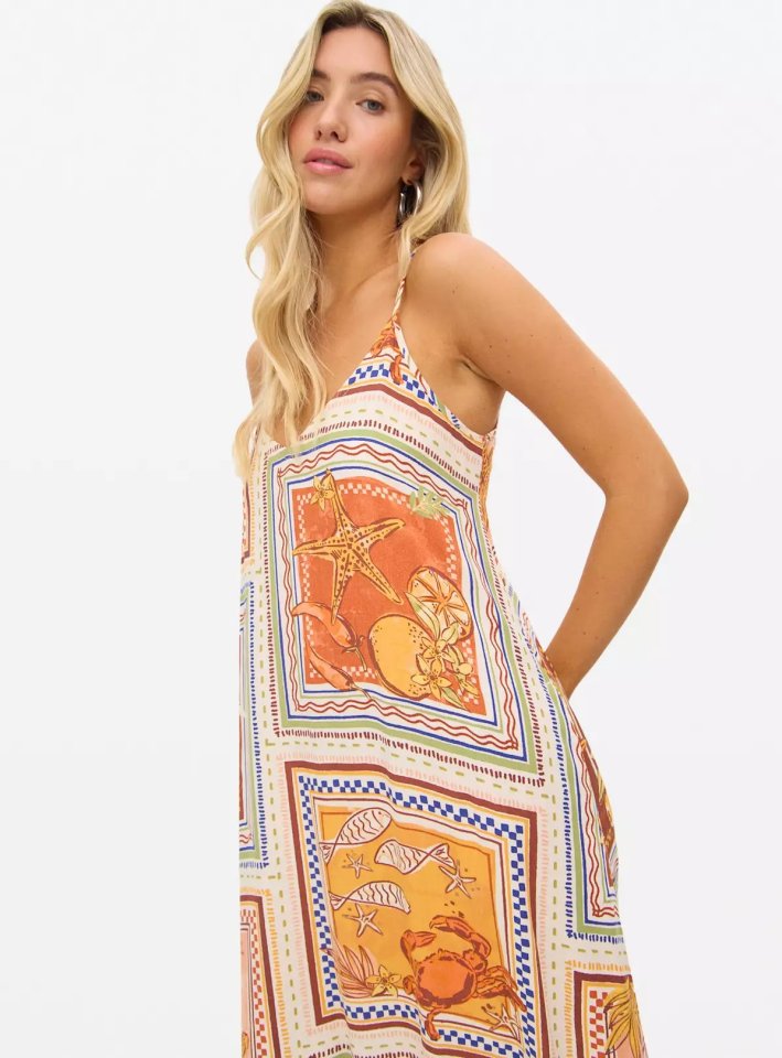 Woman wearing a sleeveless summer dress with a seashell and citrus fruit print.