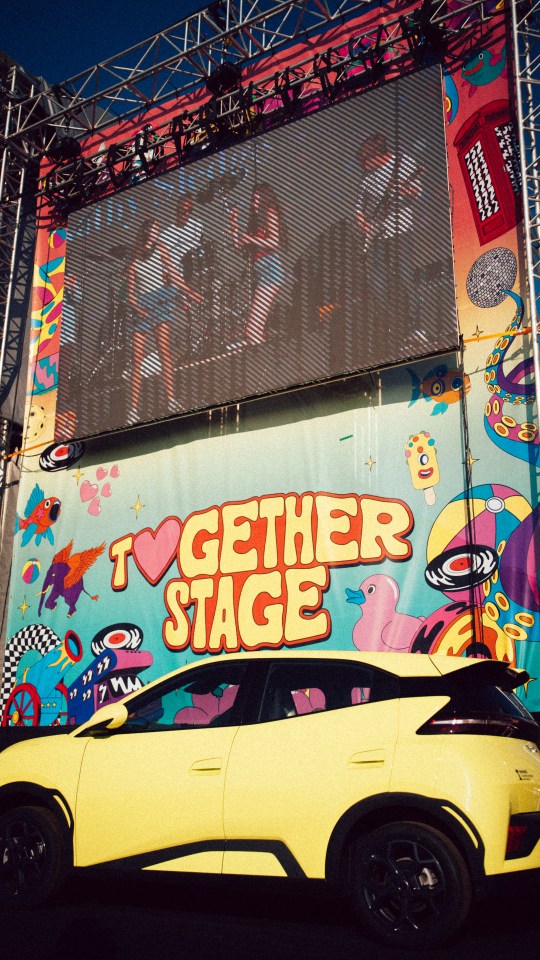 Illustration of a yellow car parked in front of a stage at the Together Again Festival.