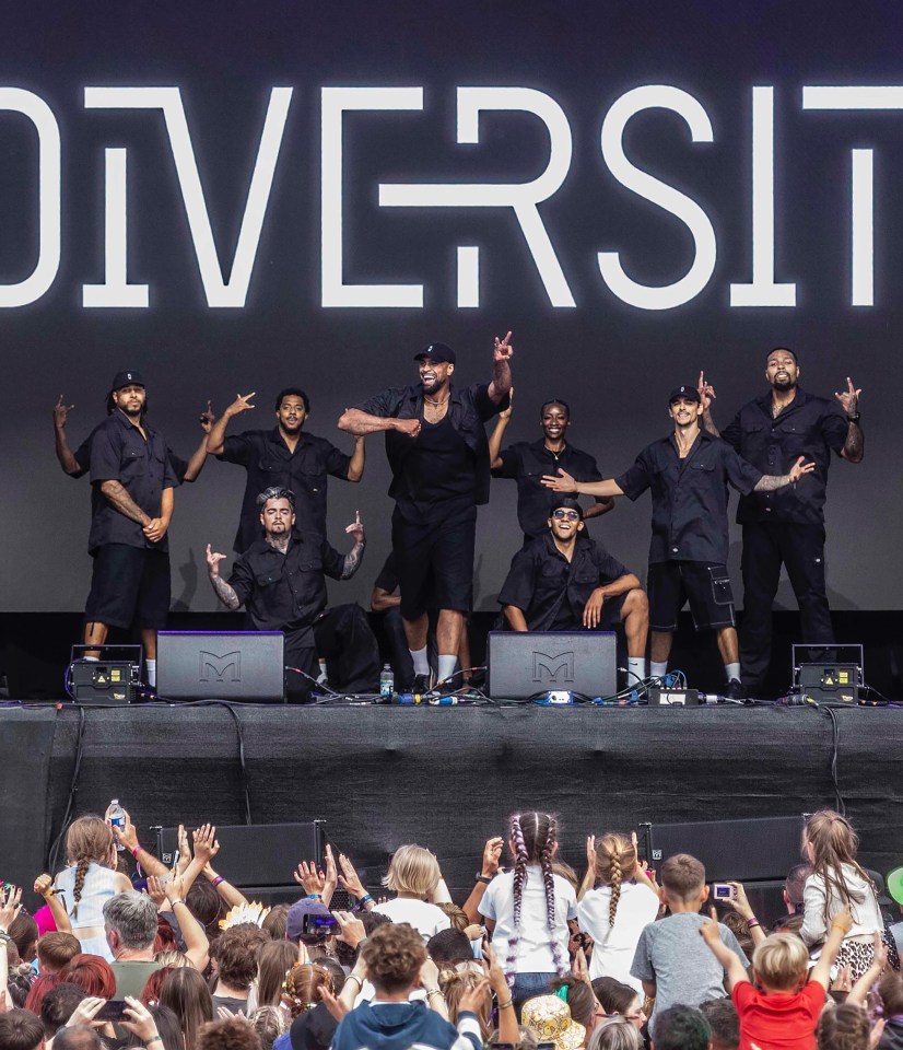 A diverse group of dancers on stage at a festival, performing in front of a large screen displaying the word "DIVERSITY".