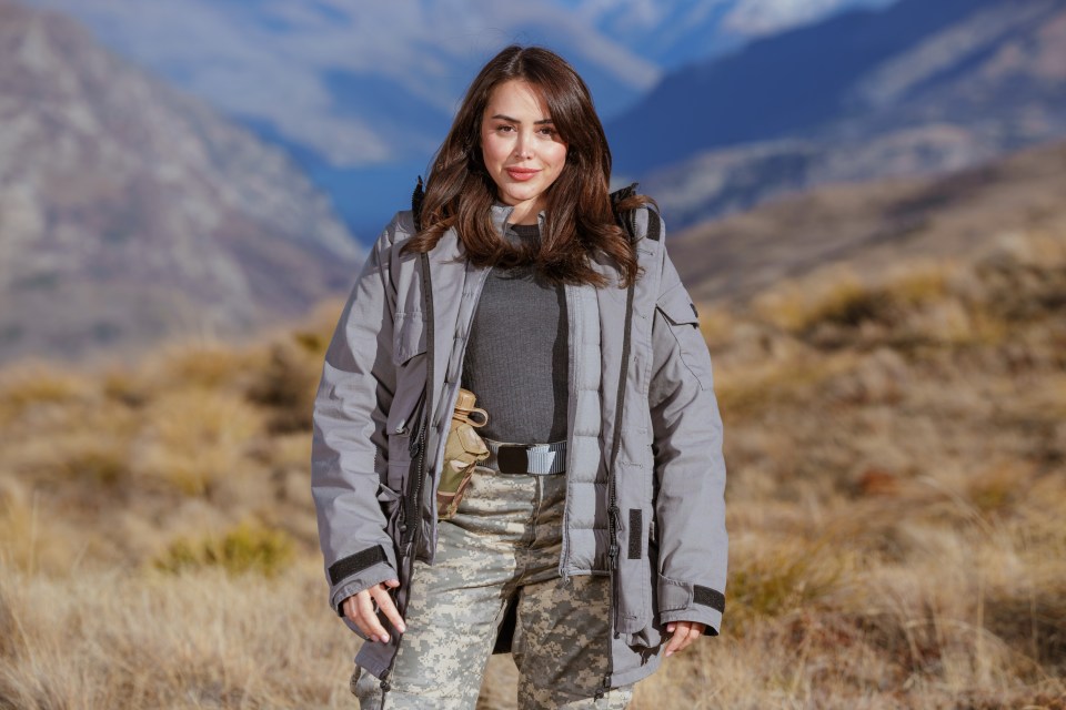 Marnie Simpson in camouflage pants and a gray jacket in a mountainous landscape.