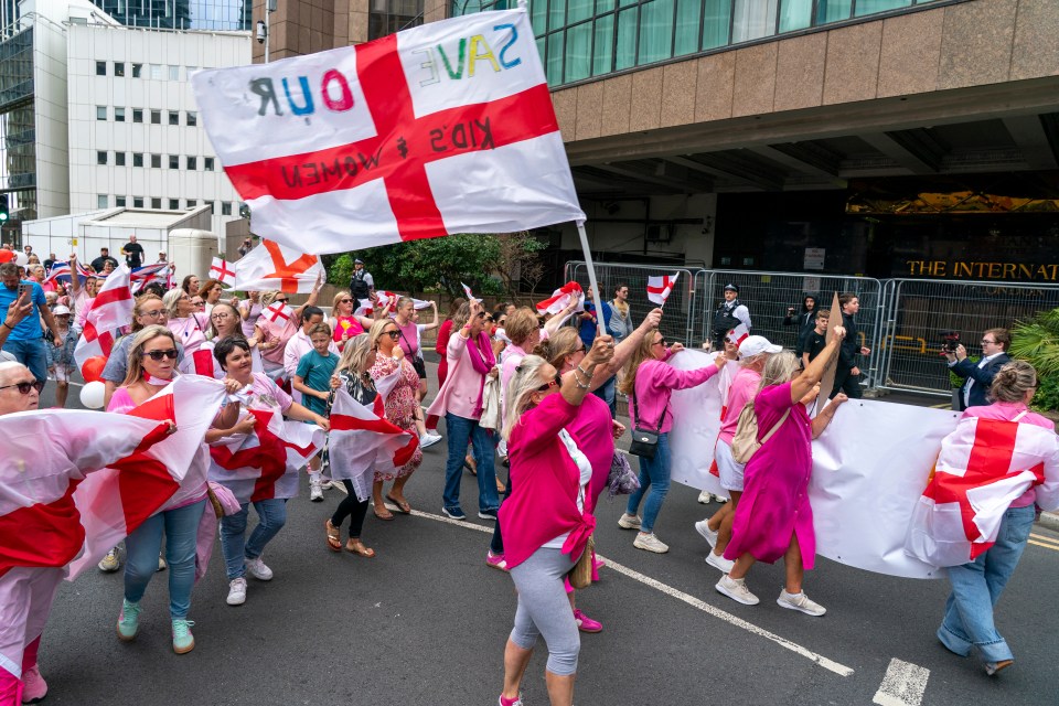 Protestors outside a hotel carrying flags that read "Save Our Kids & Women".