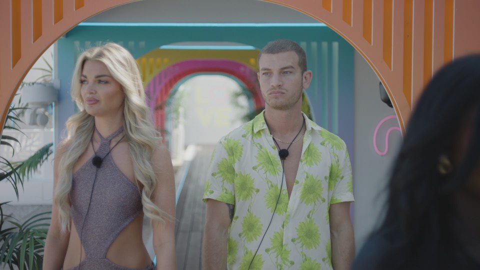 Helena and Blu from Love Island walking through a colorful archway.