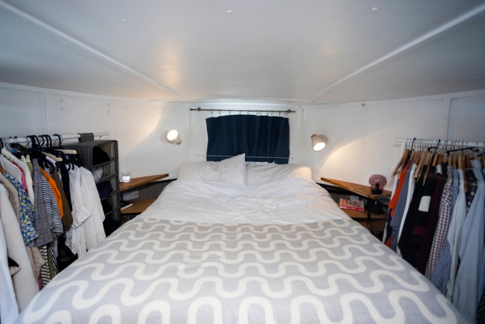 Bedroom on a houseboat with a bed and clothes hanging on racks.