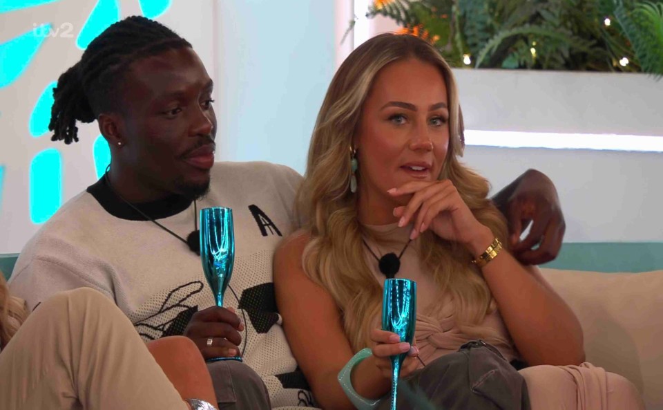 Dejon and Meg from Love Island sitting together with champagne flutes.