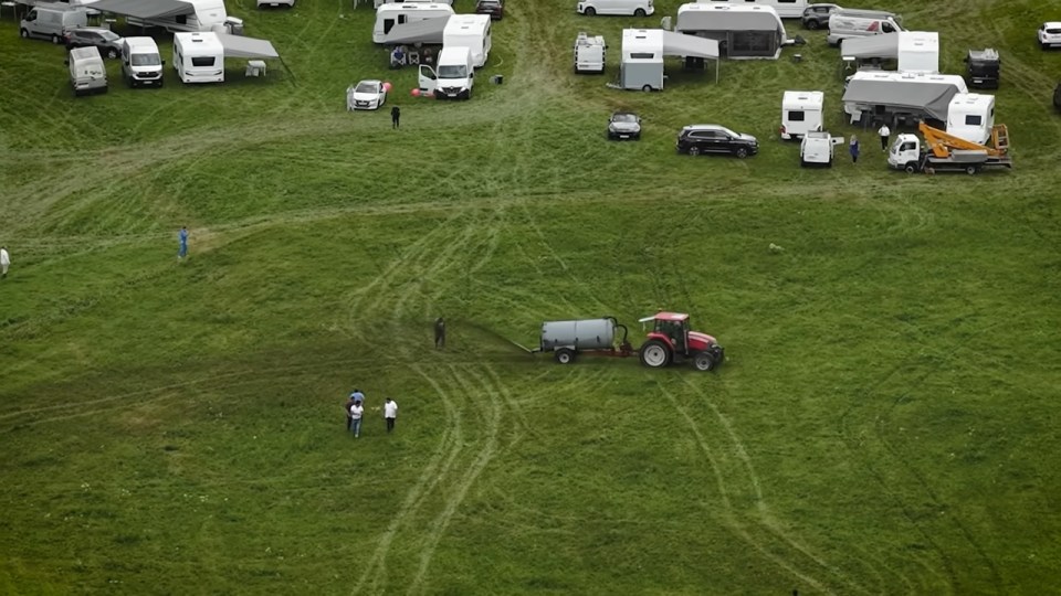 Aerial view of a tractor spreading manure on a field with several caravans parked nearby.