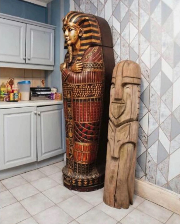 A painted sarcophagus and a carved wooden totem stand in a kitchen.