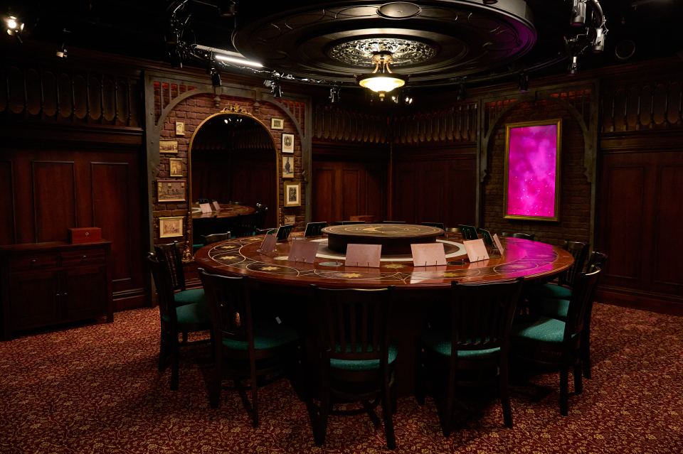 A large, round table surrounded by chairs in a dark, ornate room.